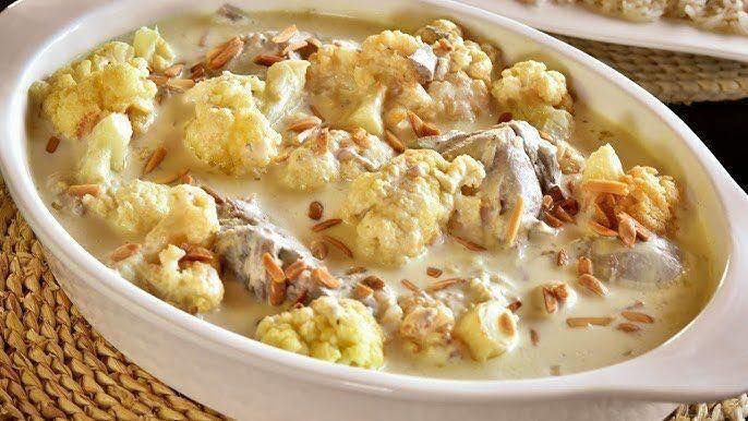 A white casserole dish filled with chicken and cauliflower in a creamy sauce.