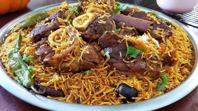 Plate of spiced rice with large pieces of meat, green chilies, and herbs; warm colors.