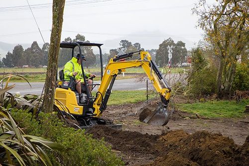 A man is driving a yellow excavator on a dirt road.