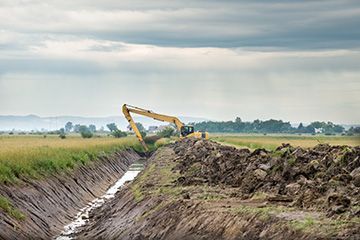 A large excavator is digging a trench in a field.