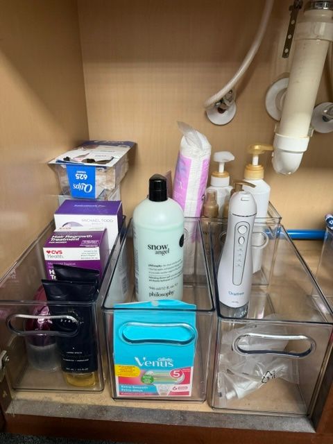Under-sink cabinet with assorted toiletries, cleaning products, and plumbing pipes.