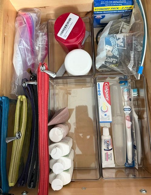 Open drawer with assorted toiletries and cosmetics organized in clear and colored cases