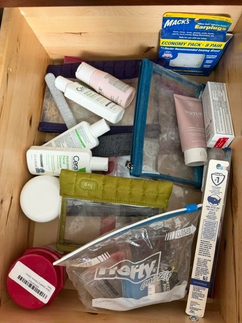 Open wooden drawer with assorted toiletries and medicine tubes, bottles, and a yellow box.