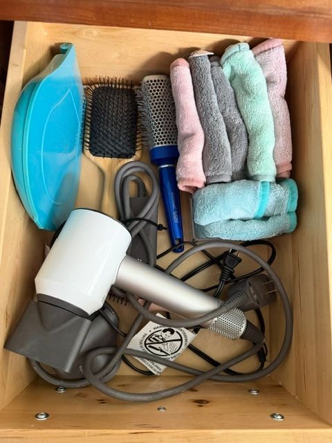 Drawer with hair dryer, round brush, combs, clips, curling iron, and rolled towels.