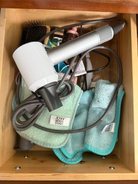 Hair dryer and cords tangled with small towels in a wooden drawer.