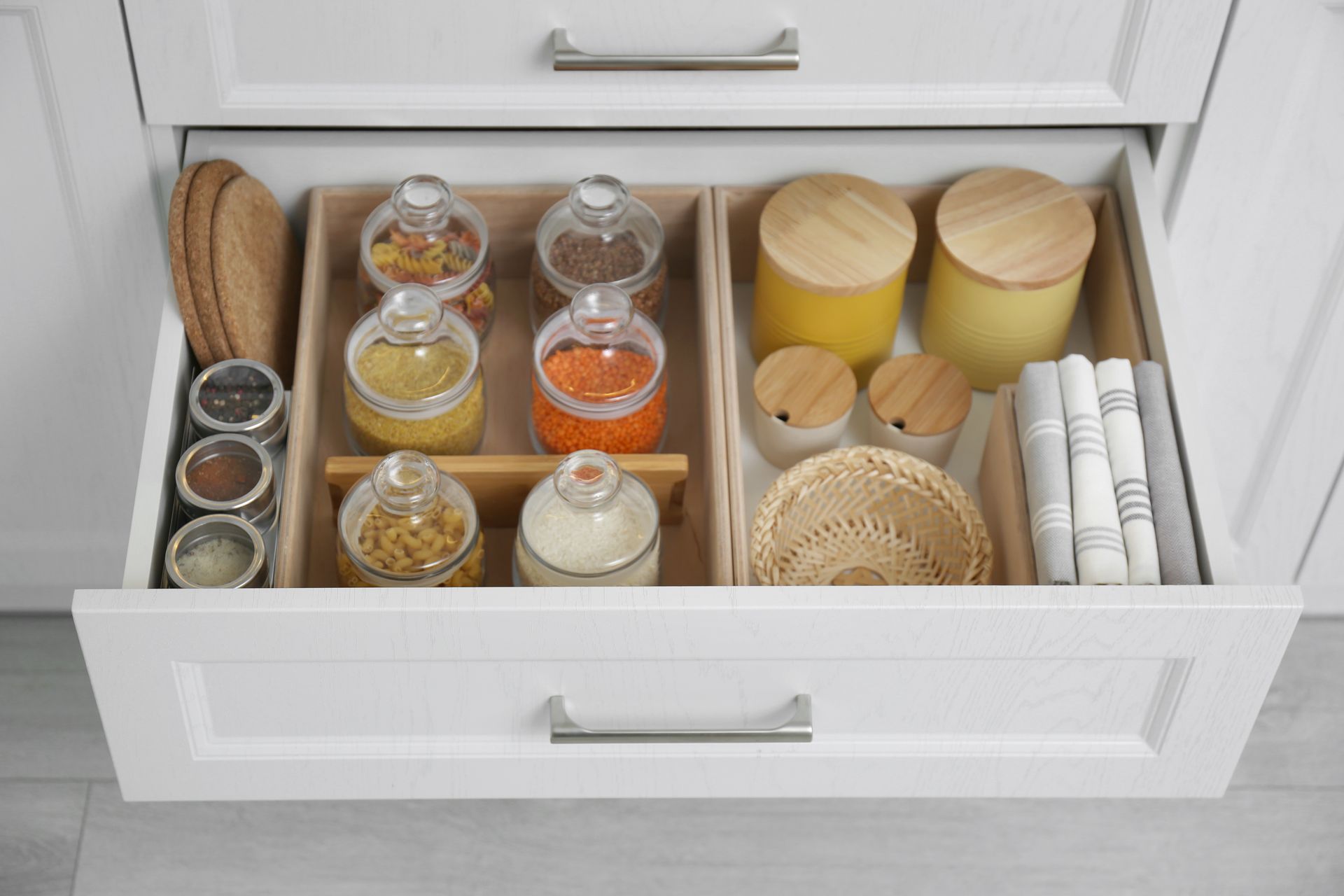 Drawer organizer with glass jars, candles, woven baskets, and folded napkins