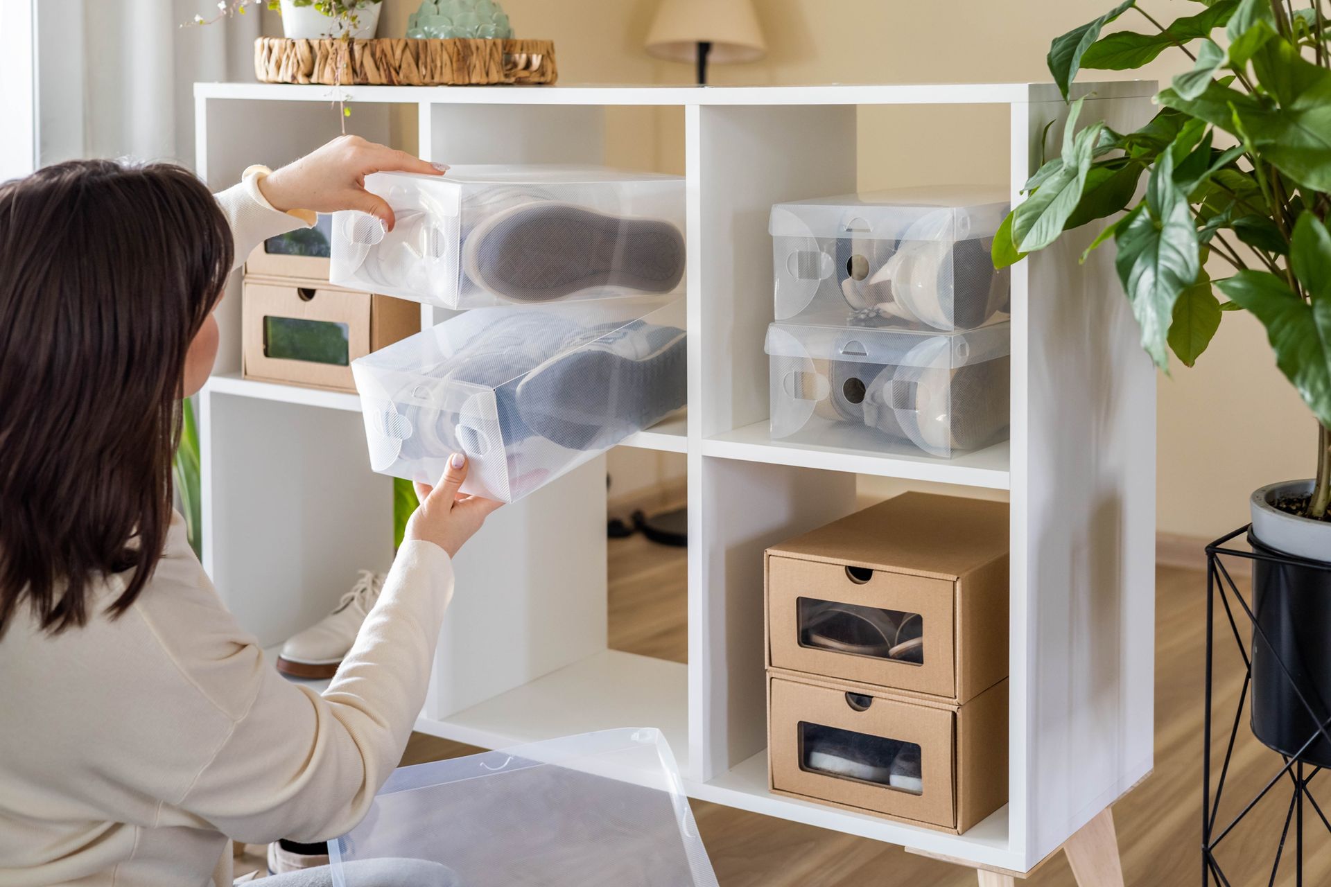 Person organizing clothes in a white cubby shelf with storage boxes in a bright room