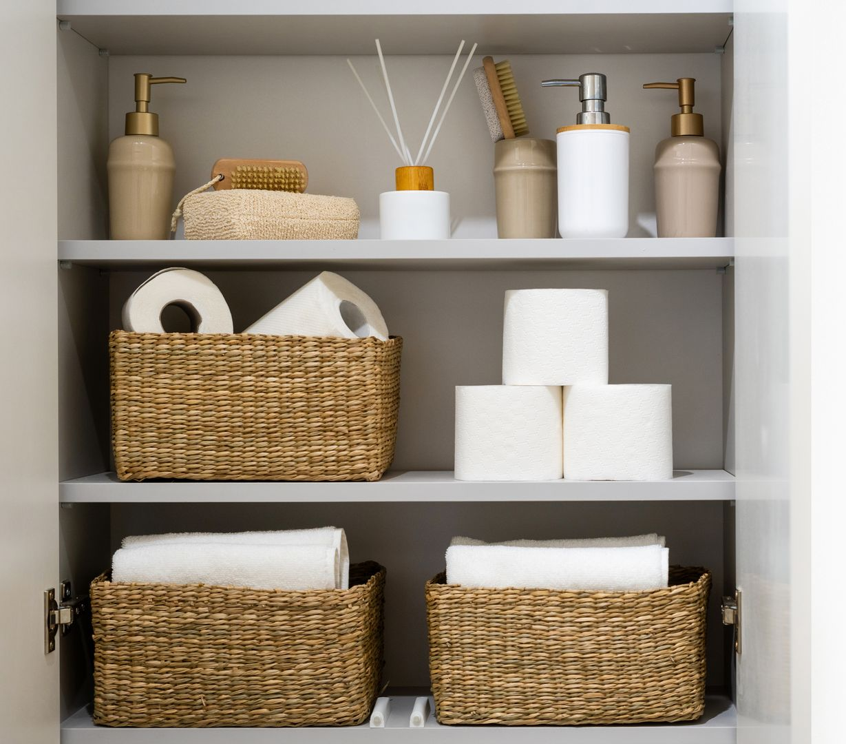 Organized bathroom shelf with wicker baskets, toilet paper, towels, and soap dispensers in neutral tones