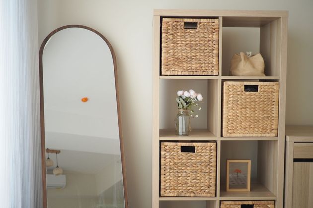 Full-length mirror beside a wooden cubby shelf with wicker baskets, flowers, and small decor items.
