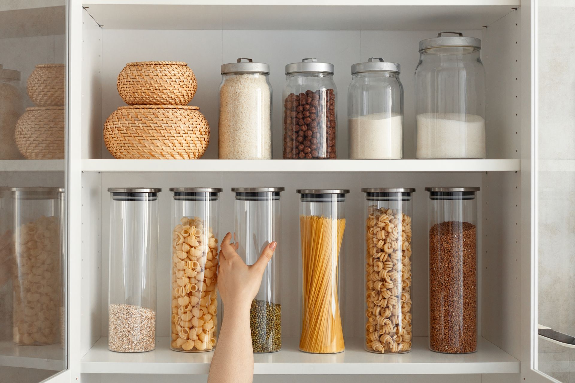 Shelf of glass jars filled with grains and beans; a hand points at the lower row.