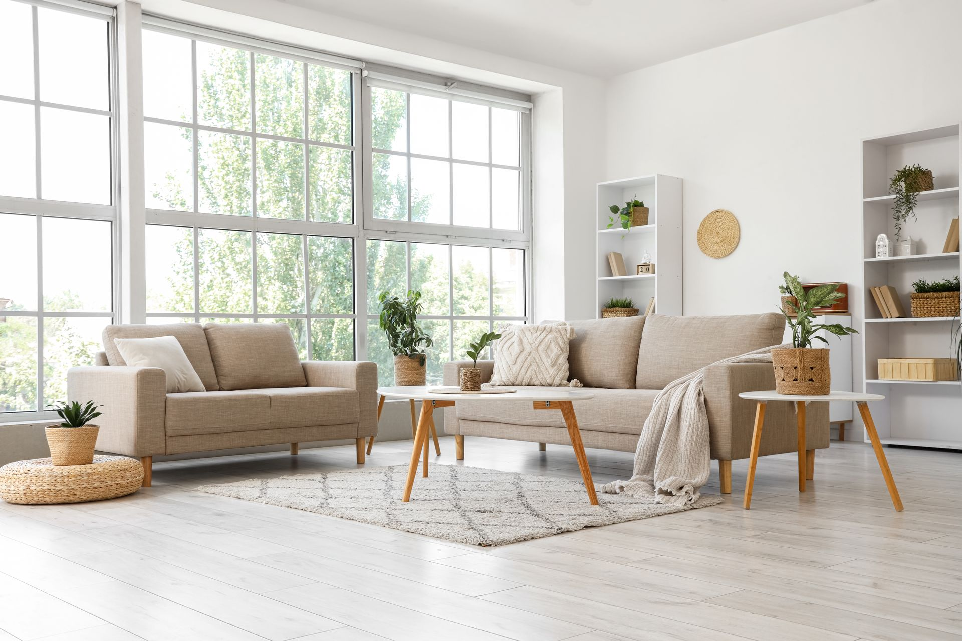 Bright, airy living room with beige sofas, wooden coffee table, plants, and large windows
