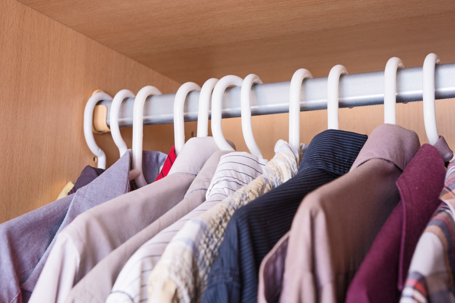 Clothes hanging on white hangers in a closet, with shirts in neutral, pink, blue, and brown tones.