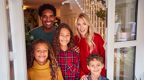 Family of five smiles from doorway, festive lighting and decorations.