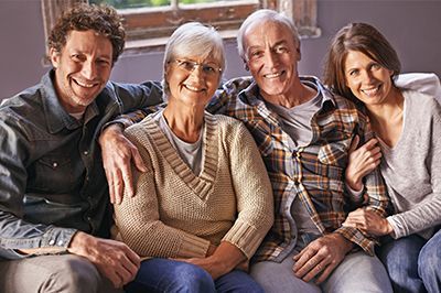 Family of four smiling on a couch: older couple with adult children.