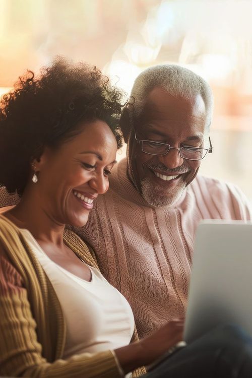 Smiling Black couple looking at a laptop together. Woman with afro, man with glasses. Soft, warm colors.