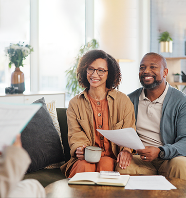 Couple smiling while reviewing documents with an advisor. Living room setting.