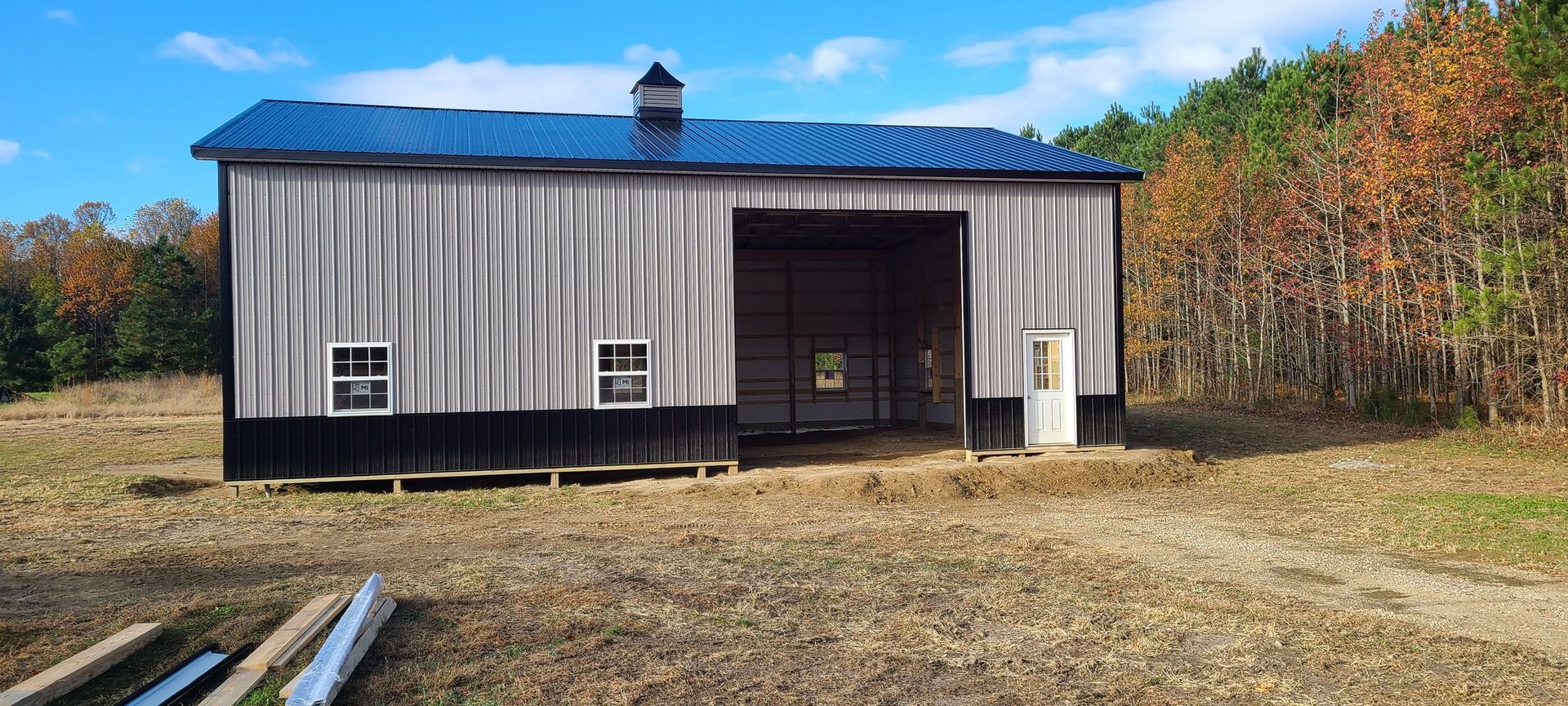A large metal building with a blue roof is sitting in the middle of a dirt field.