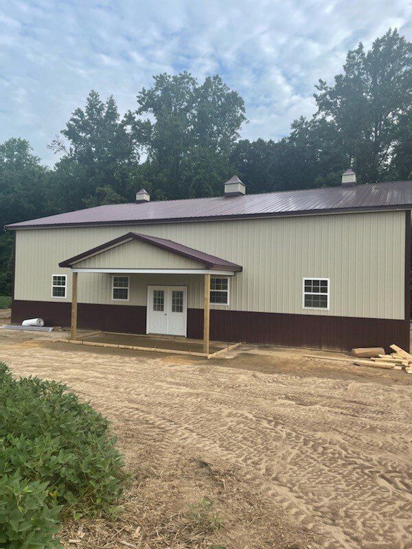A large building with a porch is sitting in the middle of a dirt field.