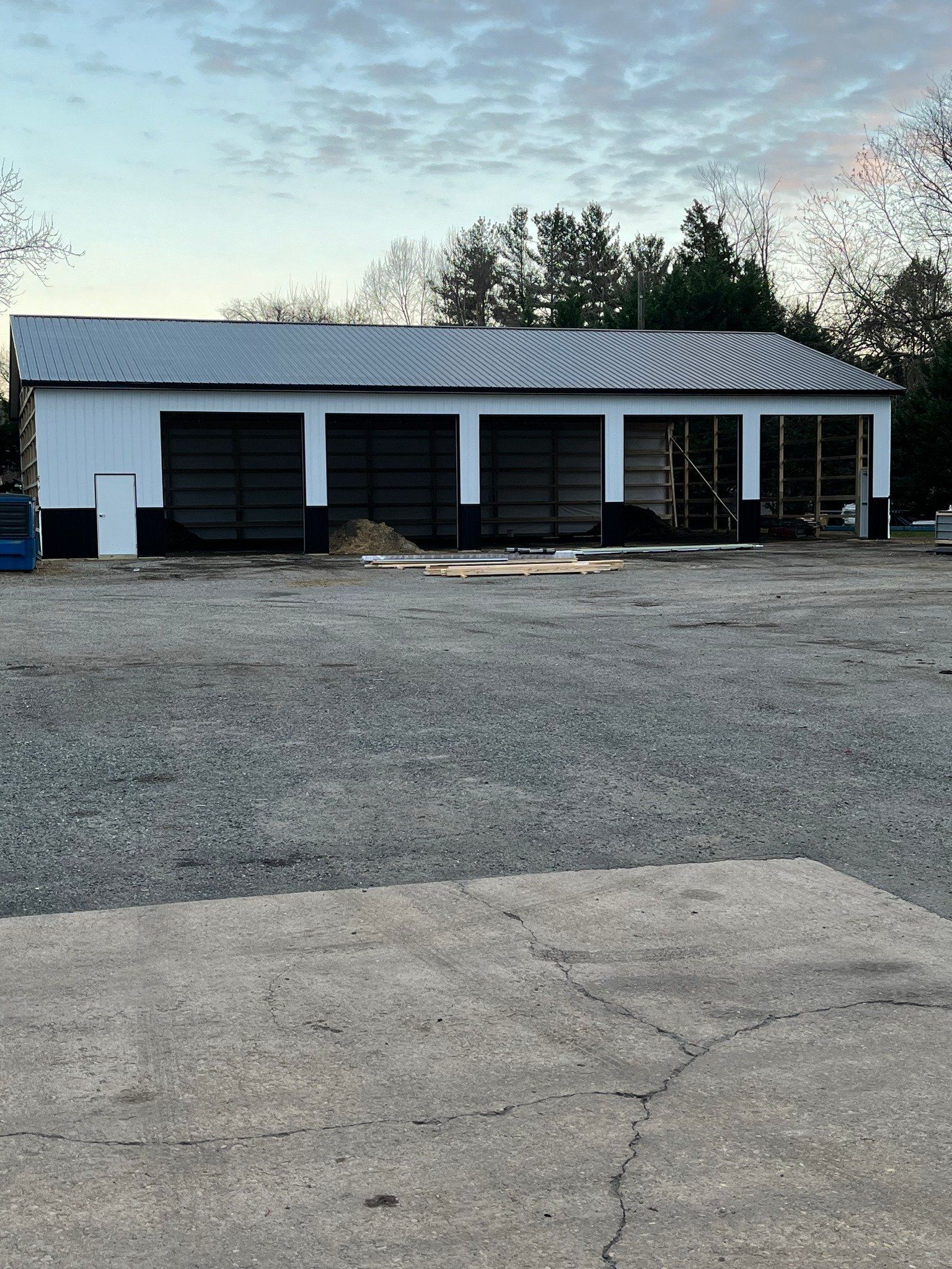 A large white building with black doors is sitting in the middle of a gravel lot.