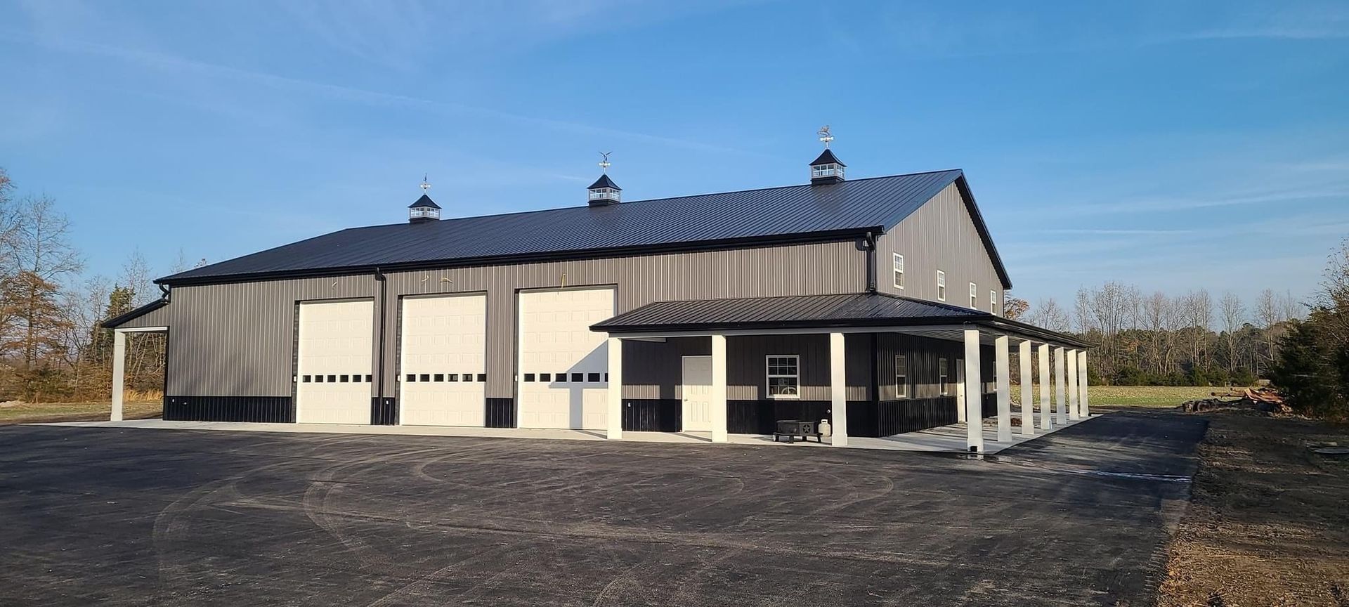 A large barn with a porch and garage doors is sitting on top of a dirt field.