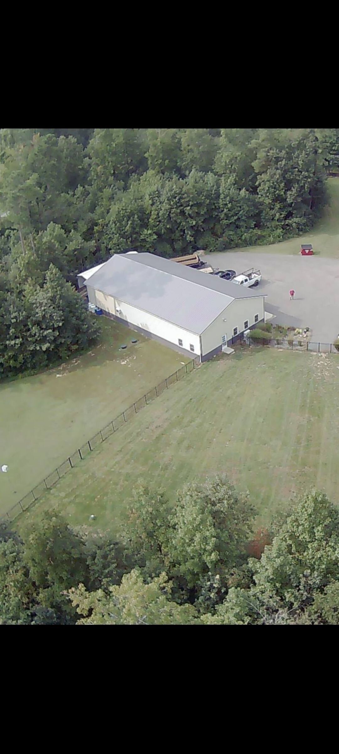 An aerial view of a large white building in the middle of a field surrounded by trees.
