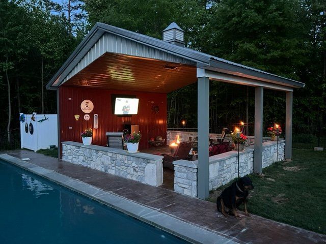 A dog is standing in front of a pavilion next to a swimming pool.