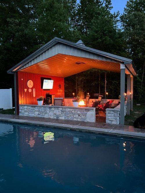 A pavilion with a fire pit and a swimming pool in the background.
