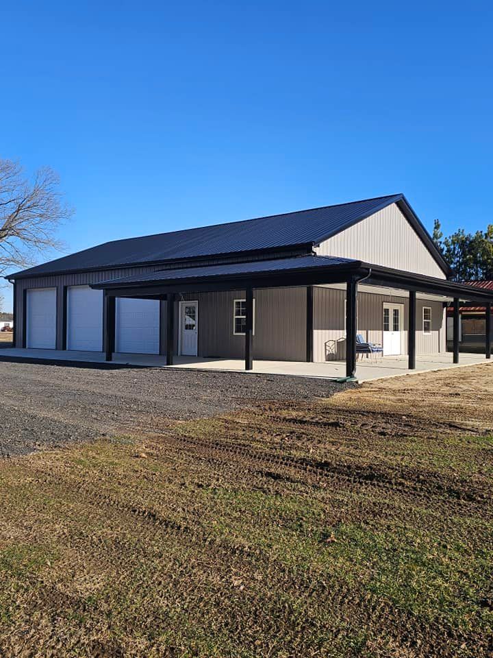A large building with a porch and a garage is sitting in the middle of a grassy field.