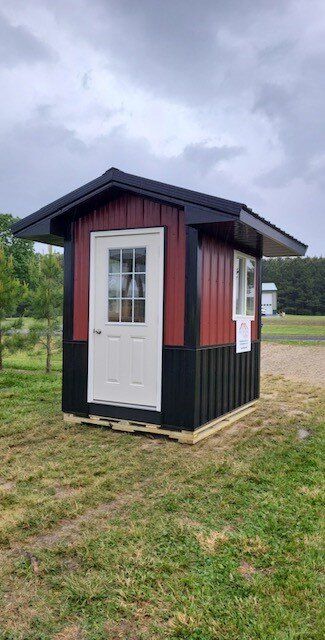A small red and black shed is sitting in the middle of a grassy field.