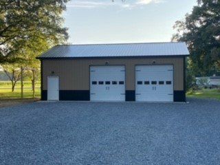 A large garage with three garage doors is sitting on top of a gravel driveway.