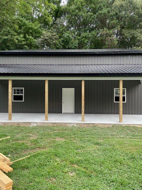 A large metal building with a porch and windows is sitting on top of a lush green field.