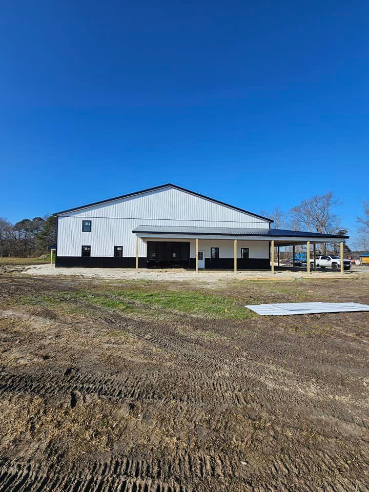 A large white building with a porch is sitting in the middle of a dirt field.
