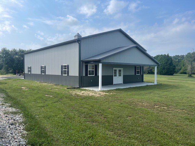 A large metal building with a porch is sitting in the middle of a grassy field.