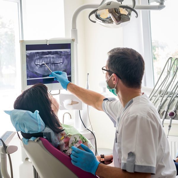 Dentist pointing at an X-ray while treating a patient in a bright dental clinic