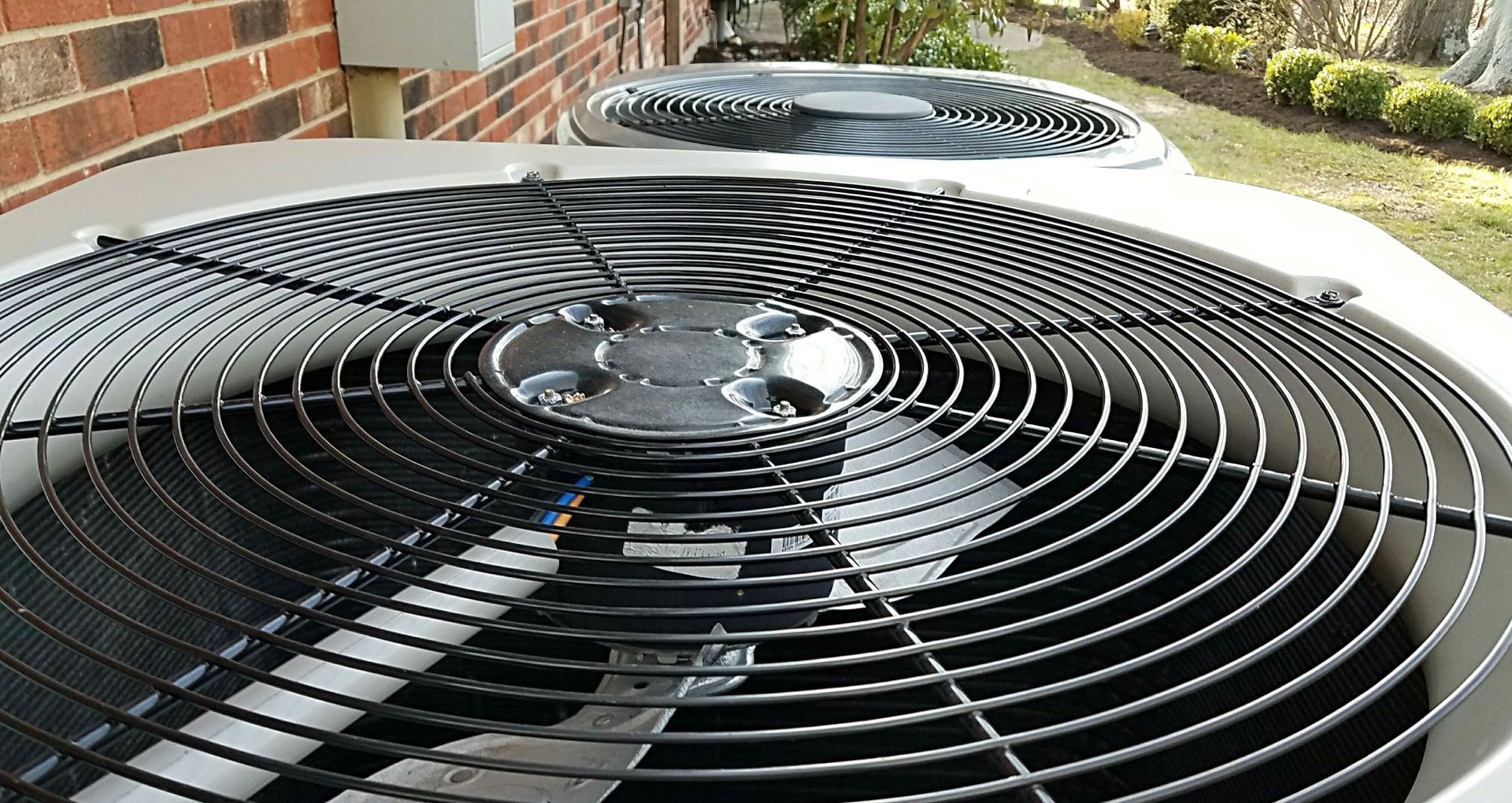 Two air conditioners are sitting on the side of a brick building.