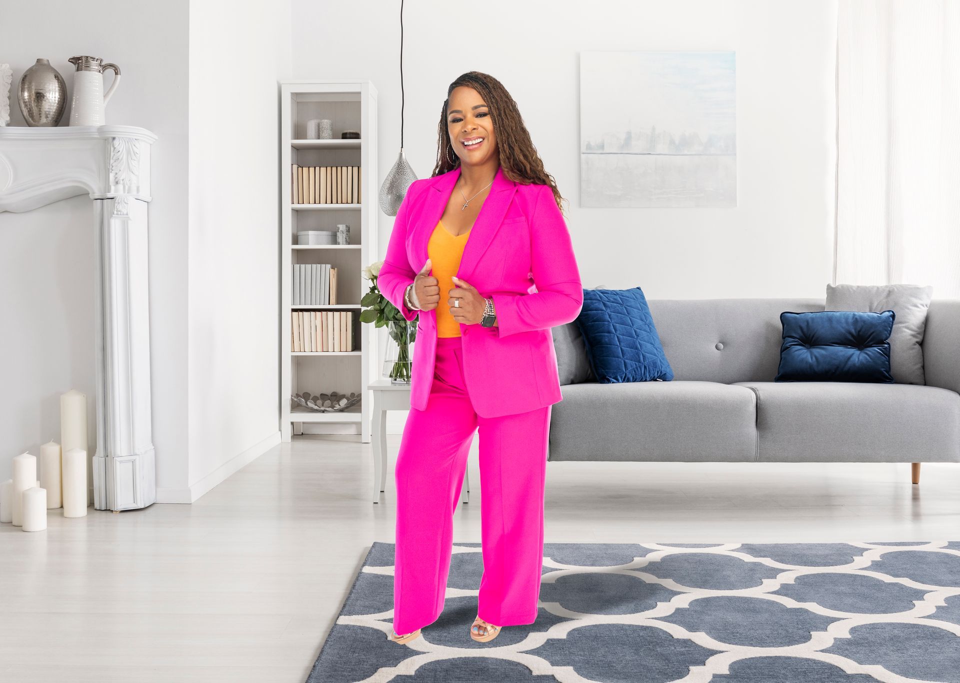 A woman in a bright pink suit is standing in a living room next to a couch.