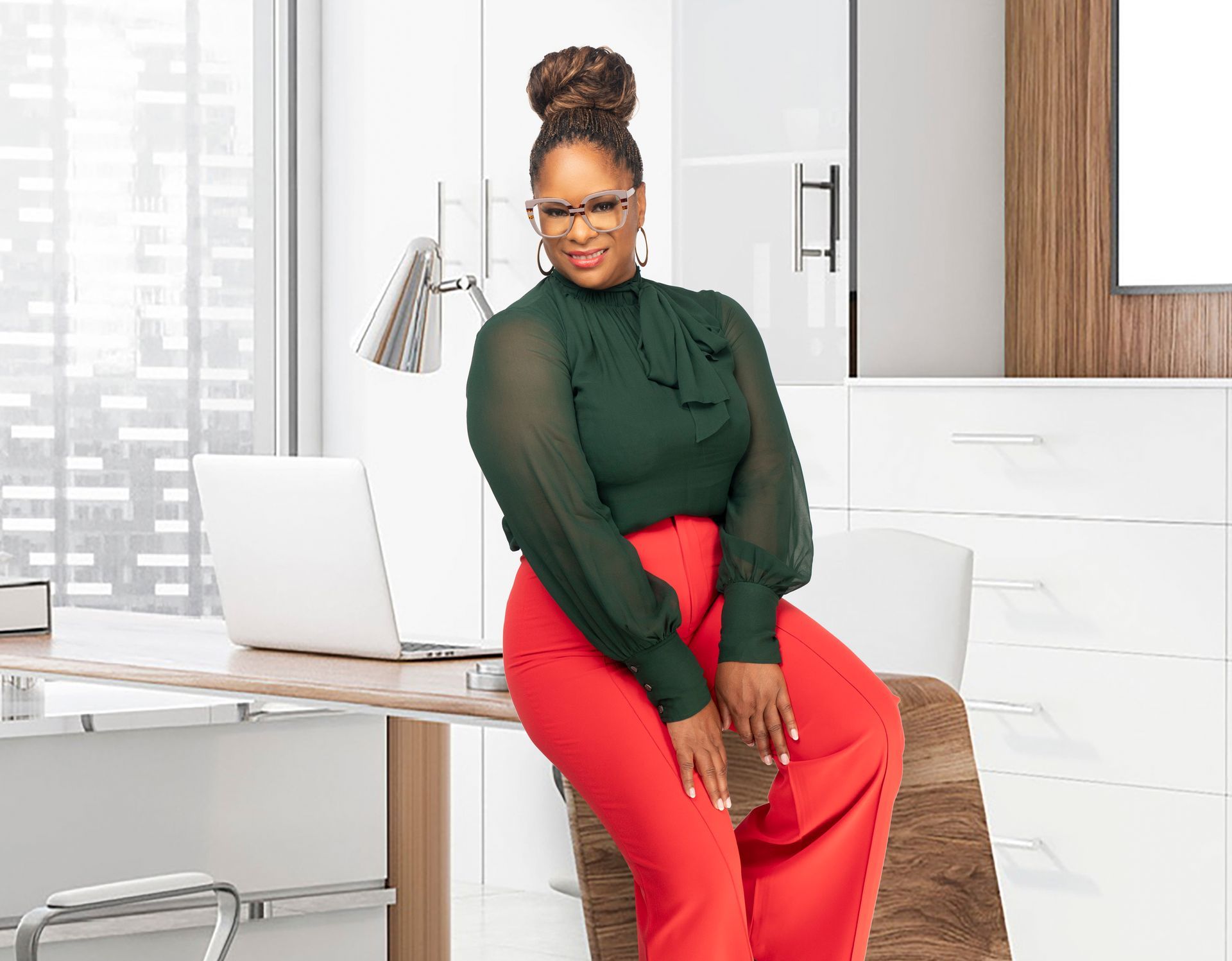A woman is sitting on a chair in front of a desk with a laptop.