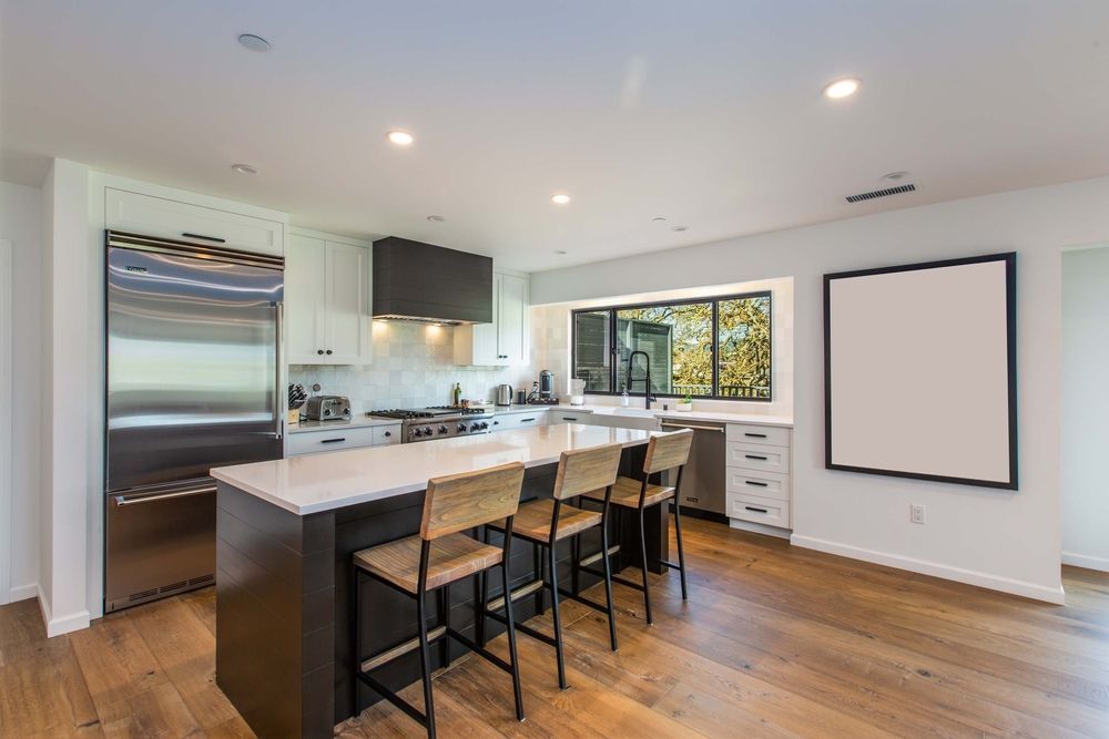 A kitchen with a large island and stools and a white board on the wall.