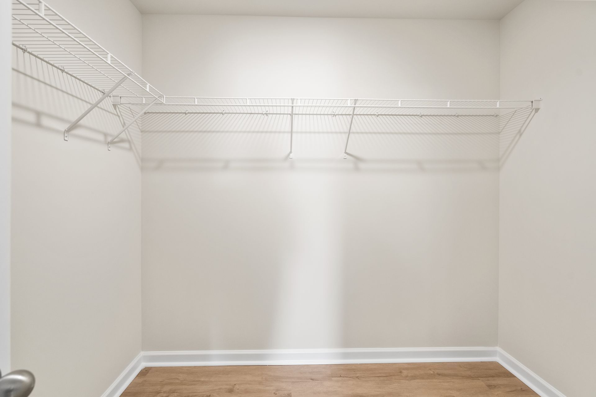 An empty walk in closet with wooden floors and wire shelves.