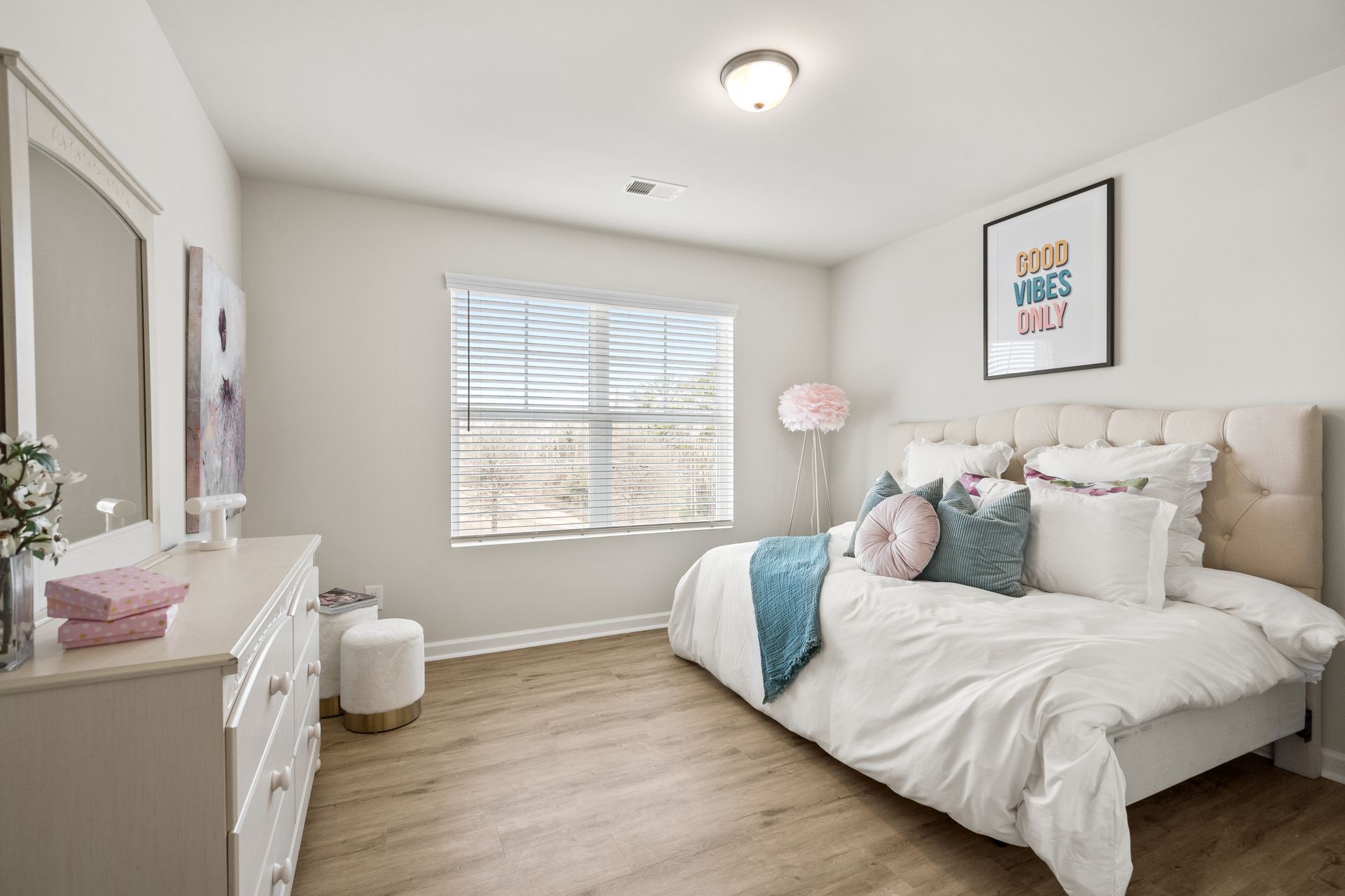 A bedroom with a large bed , dresser , mirror and window.