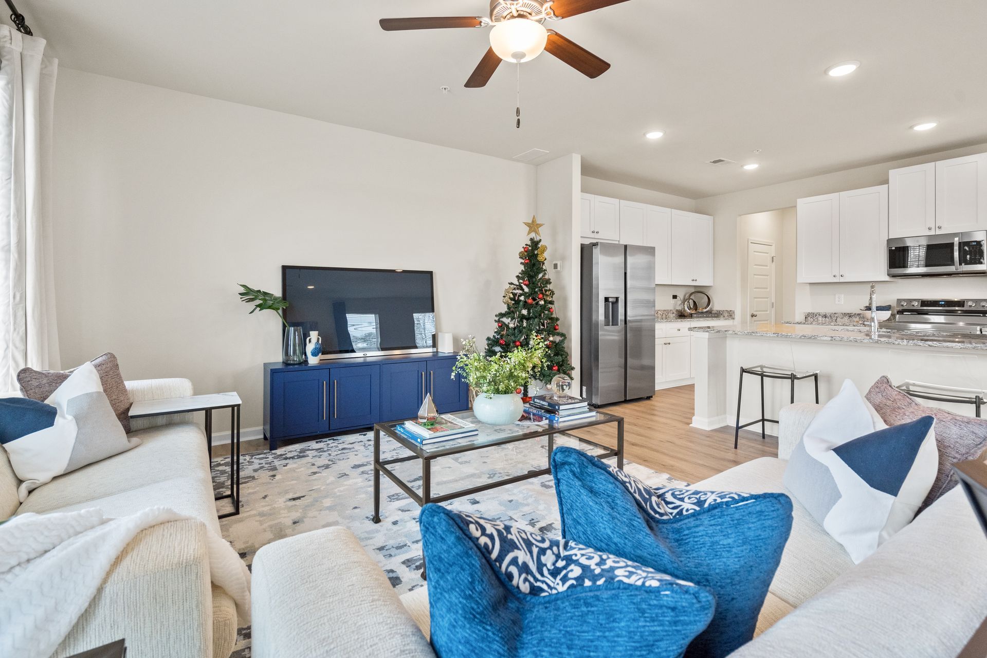 A living room with a christmas tree in the background and a ceiling fan.