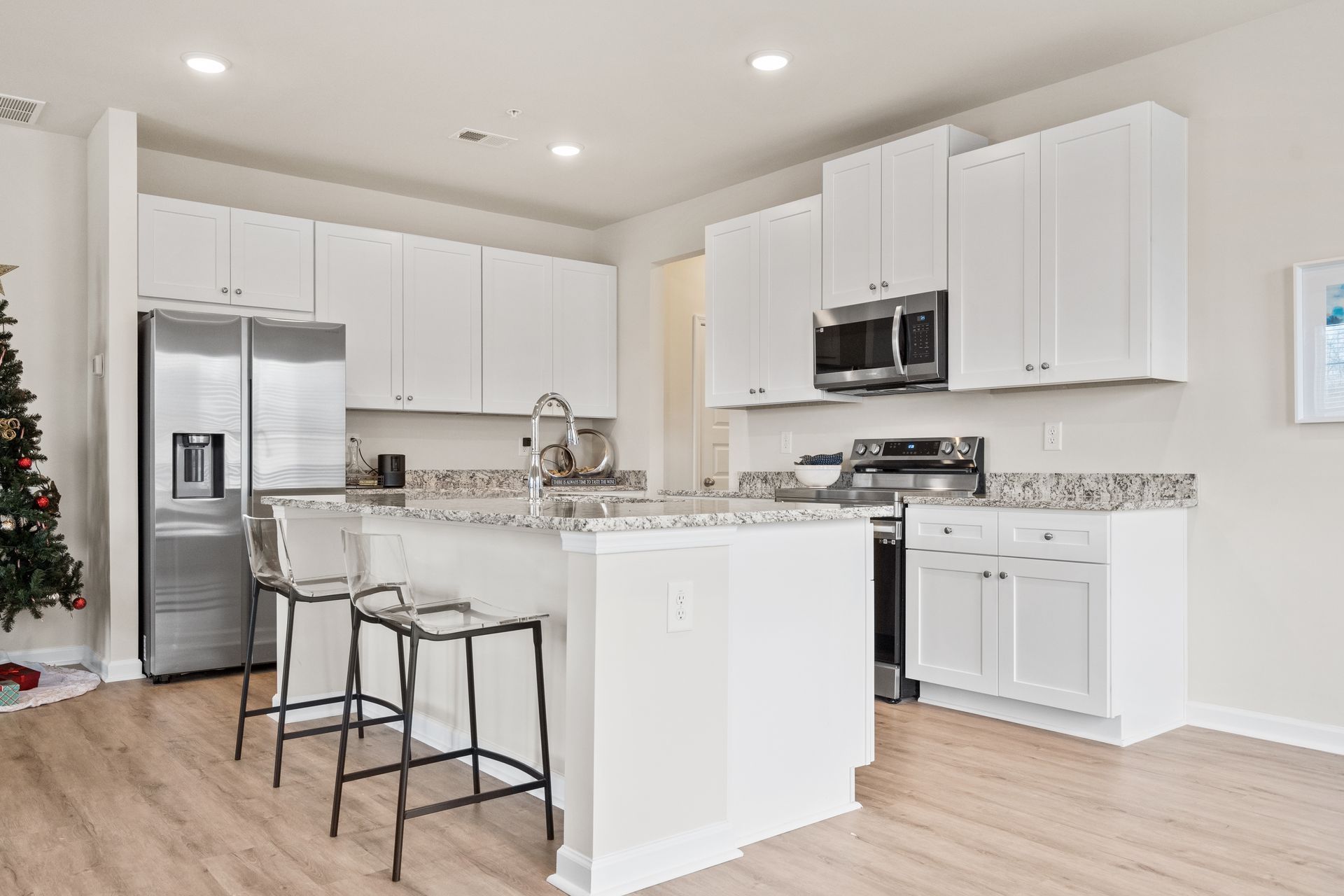 A kitchen with white cabinets and stainless steel appliances and a christmas tree in the background.