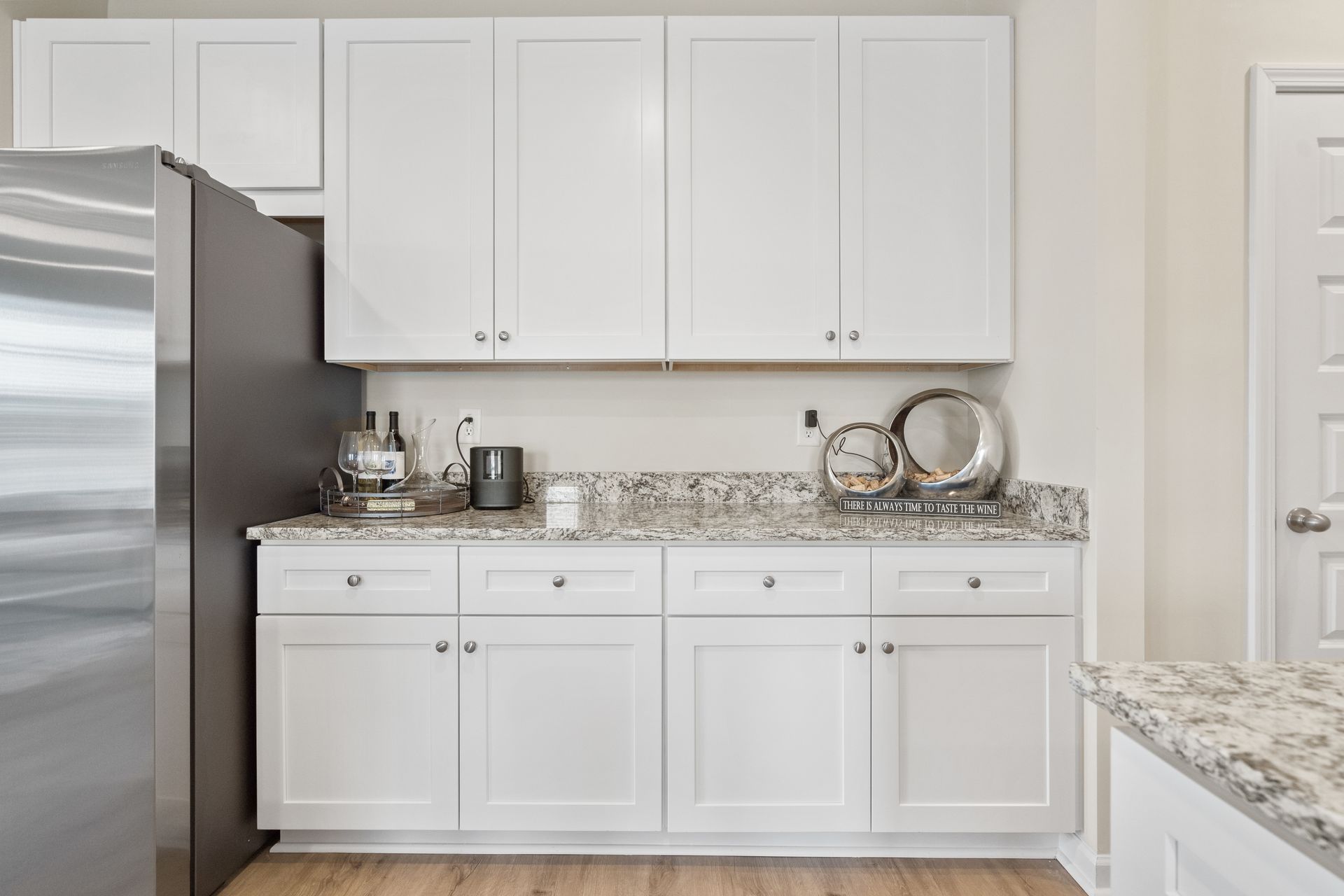 A kitchen with white cabinets , granite counter tops , and a stainless steel refrigerator.