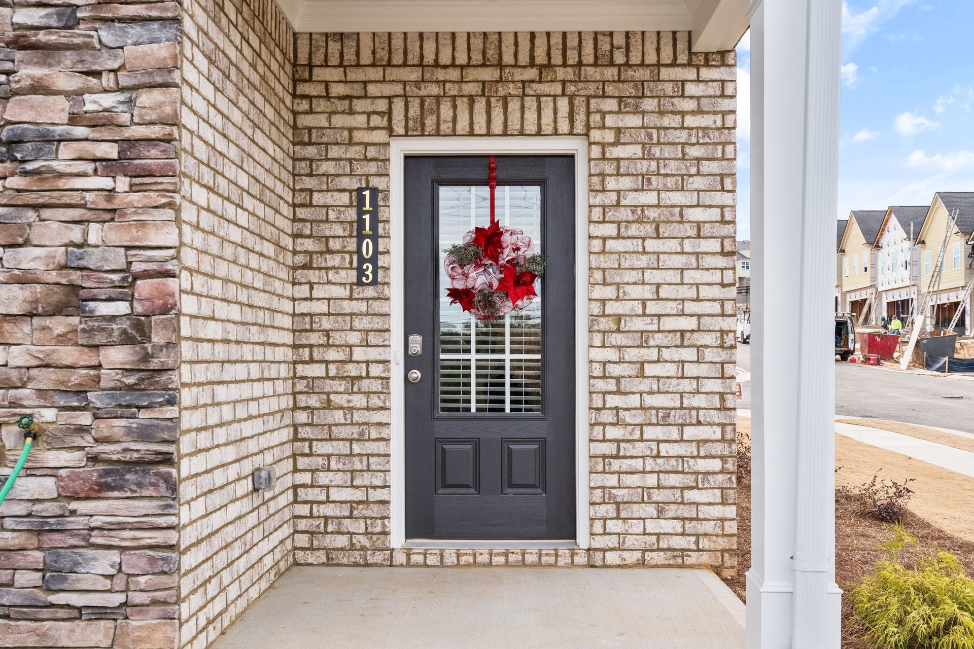 The front door of a brick house with a black door and a wreath on it.