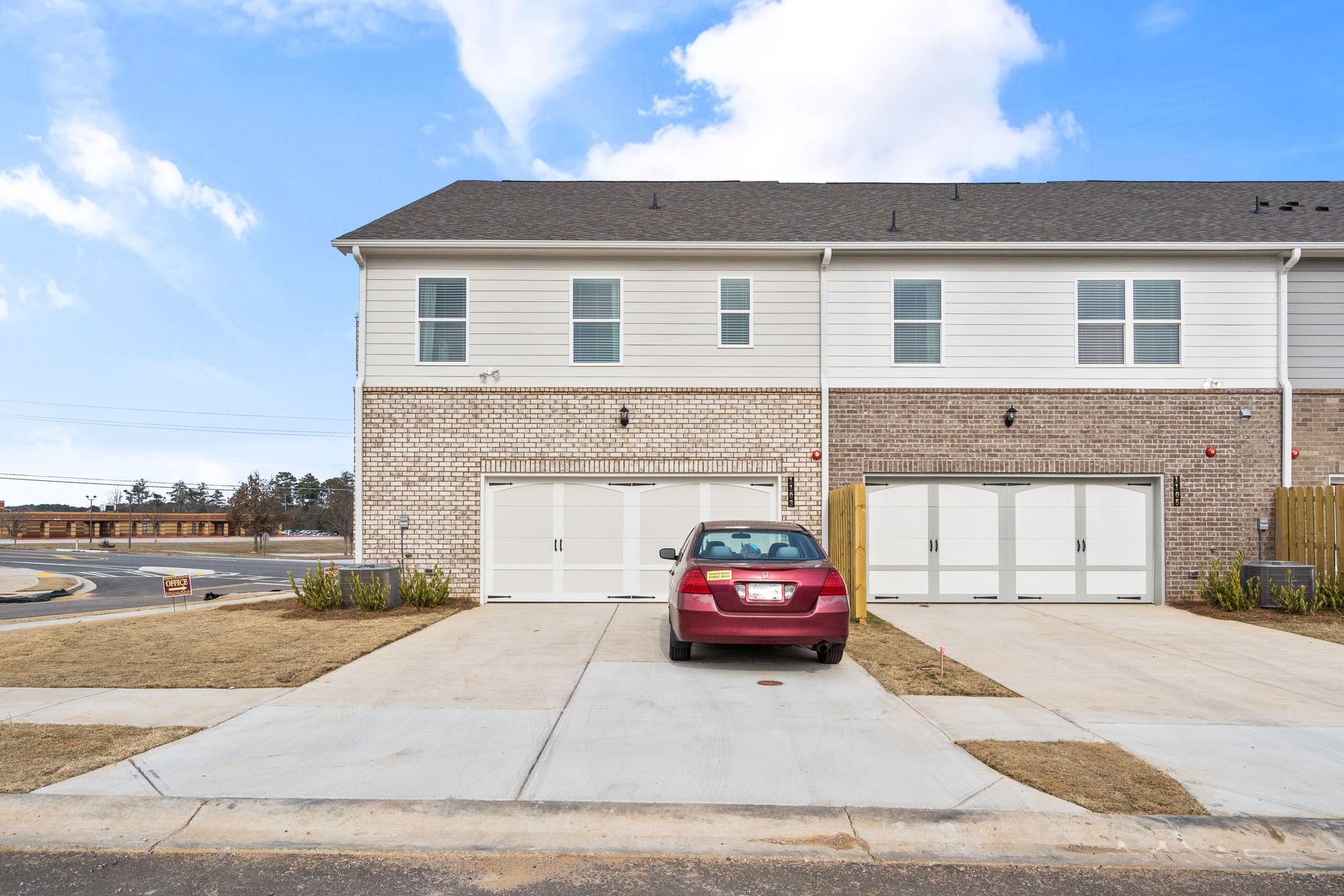 A red car is parked in front of a brick house.