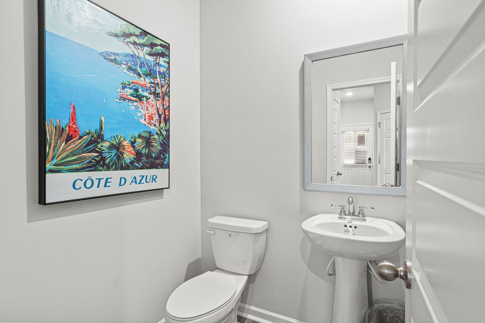 A bathroom with a toilet , sink , mirror and painting on the wall.