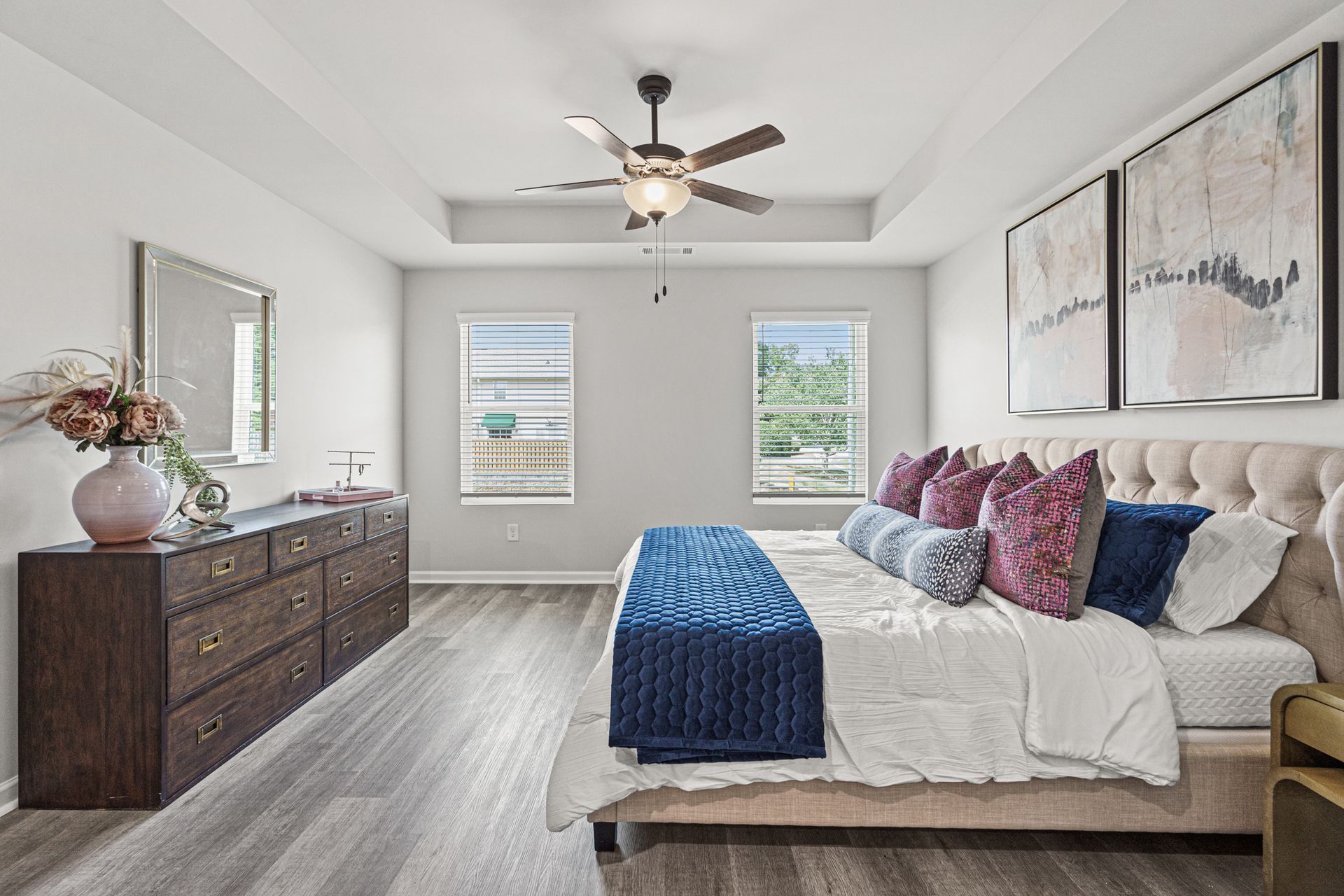 A bedroom with a bed , dresser , mirror and ceiling fan.