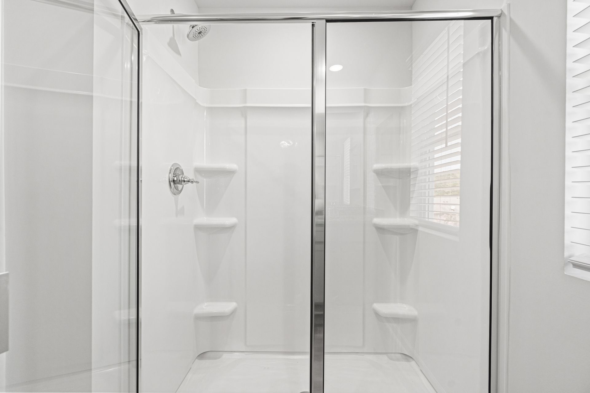 A bathroom with a walk in shower with sliding glass doors and shelves.