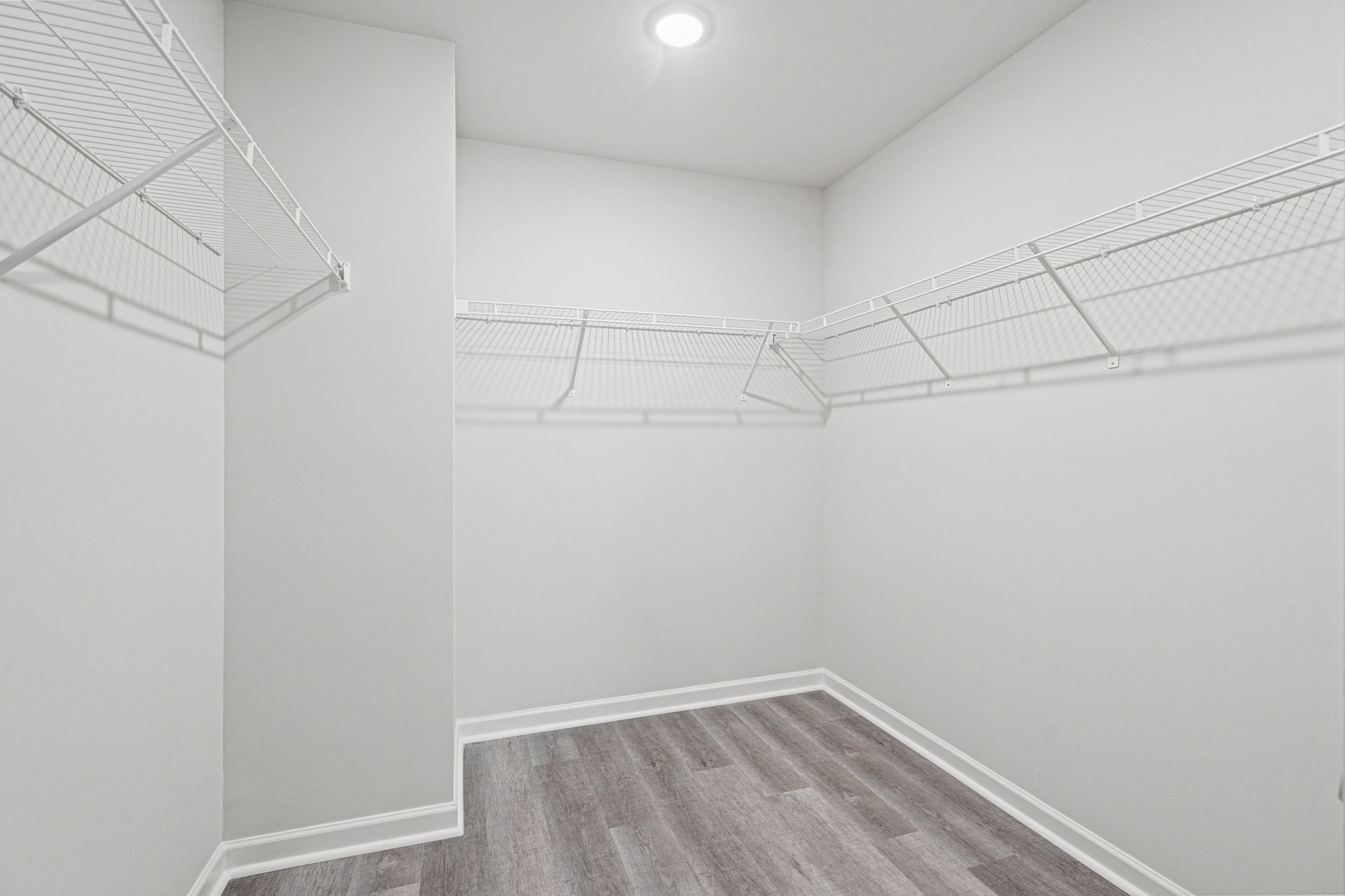 A walk in closet with a wooden floor and white shelves.