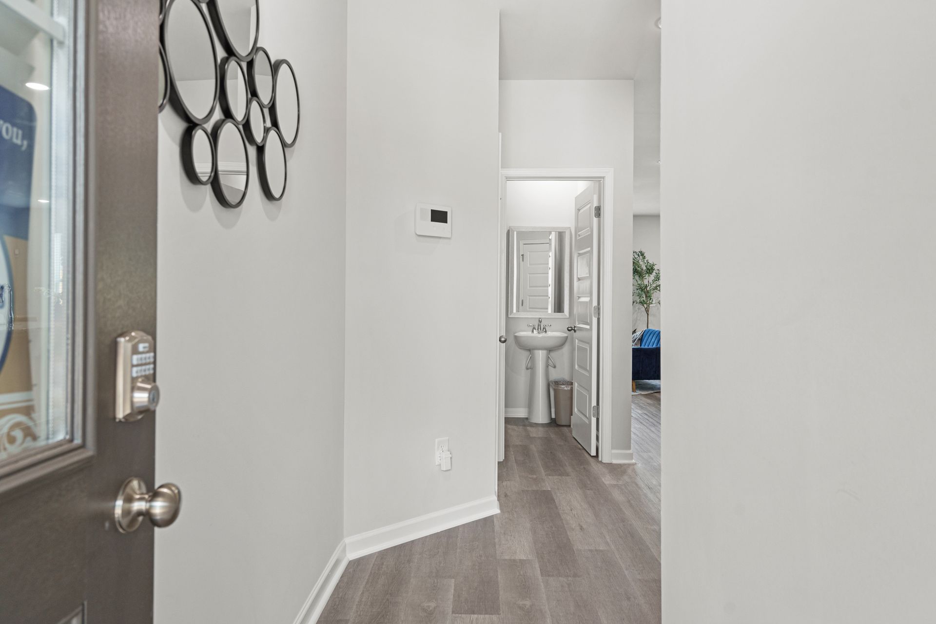 A hallway with hardwood floors leading to a bathroom and a sink.